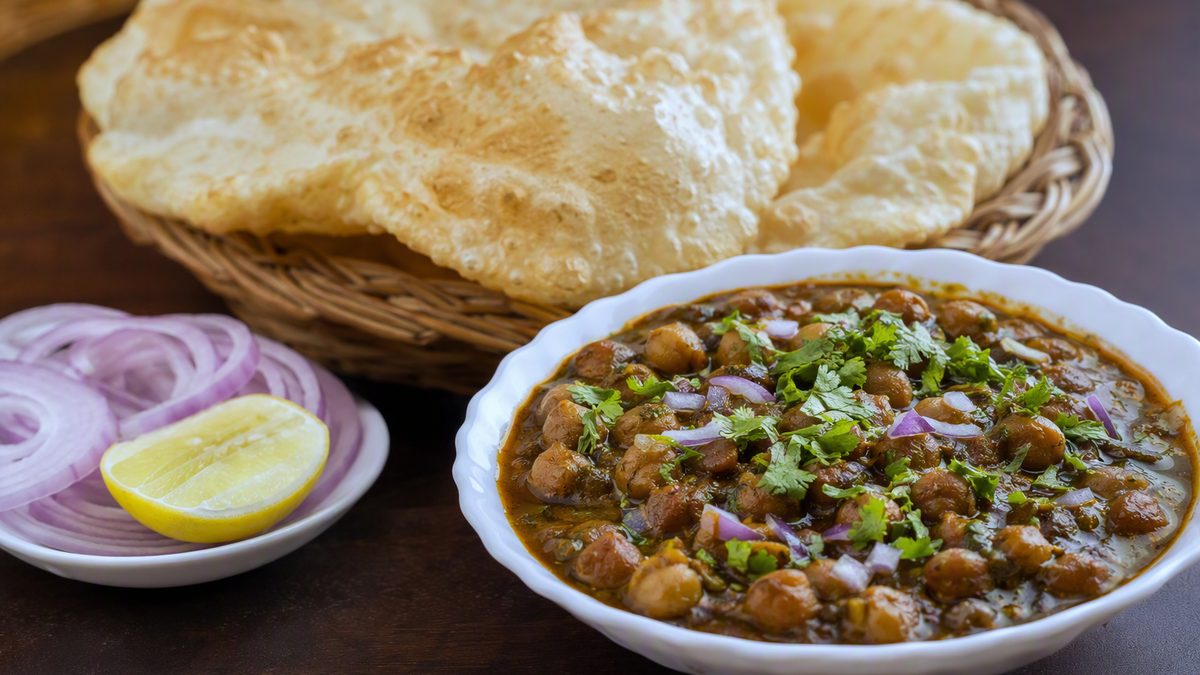 Bowl of chole with bhature and onion, lemon wedge