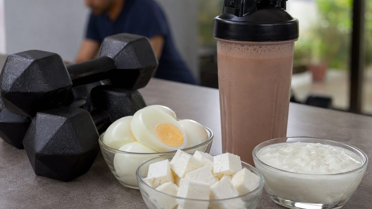 Post-workout high-protein meal of eggs, paneer, curd and a protein shake next to dumbbells